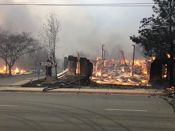 A sign saying "Welcome to Paradise" stands next to a burning building.