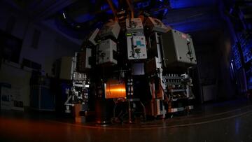 Large scientific instrument with metal boxes around the outside fills a darkened room. 