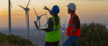 Young maintenance engineer team working in wind turbine farm at sunset