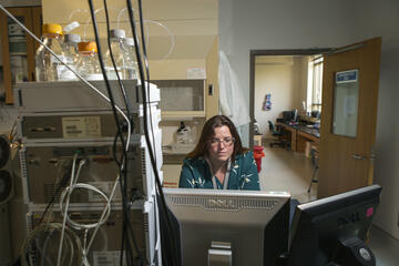 Photograph of a woman studying a computer monitor, seated in a laboratory.