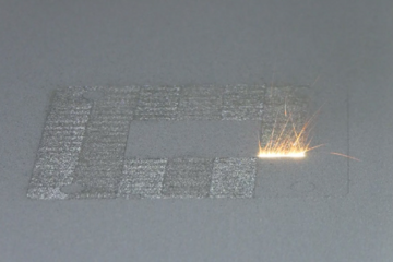 A high-power laser spot scans back and forth over a layer of cobalt-chrome powder on NIST's powder bed fusion additive manufacturing machine. Where it touches, the powder melts and fuses to underlying layers until a fully dense 3D metal part is formed. The laser travels back and forth so fast that, in this still image frame, it appears to form a white hot stripe about 10 millimeters wide.