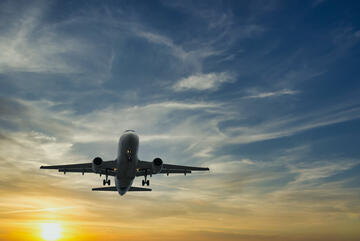 A passenger airplane seen from below takes off in front of a setting sun. 