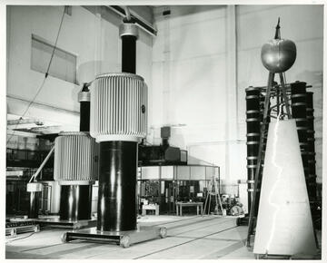 Historical photo shows a large lab space with cylindrical metal towers of different shapes. 