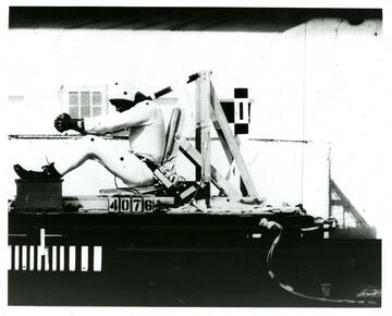 Historical photo shows test subject in helmet and bodysuit strapped into moving seat.