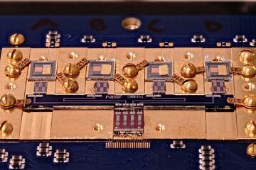 Circuit board with various square chips and gold screws. Small letters in the center say: NIST True Bq.