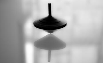 Black and white image of a spinning top on a mirrored surface.