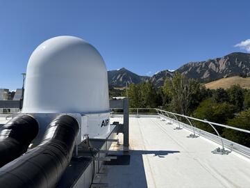 A white dome is installed on the roof of a building with mountains in the background. 