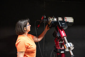 Susana Deustua looks at a large, red telescope located in a dark room. 