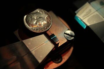 A dime for scale rests on metal base with a tiny black chip showing a bright blue laser line.