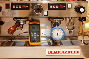 Commercial espresso machine with La Marzocco label has additional device hooked up with screen reading 201.1.