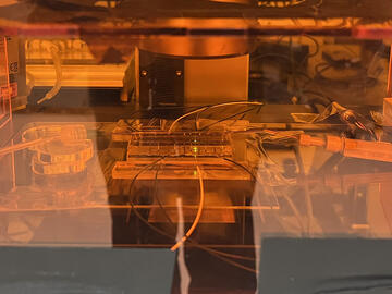 Bathed in orange light, a flowmeter is a rectangular device hooked up to clear tubes on either side. 