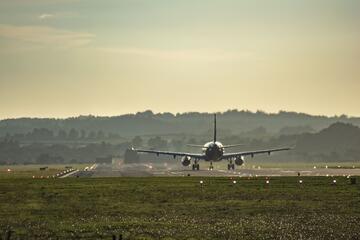 A large passenger airplane, seen from behind, sits on a runway with hills in the background. 
