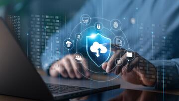 Illustration shows cloud, cybersecurity and identity icons floating over an open laptop with a person's hands at the keyboard.