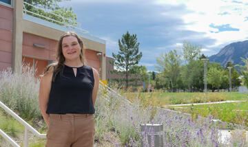 Image of a female researcher standing in front of a building with mountains in the background. 