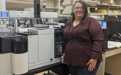 Cheryle Beuning poses in front of scientific equipment, wearing safety goggles.