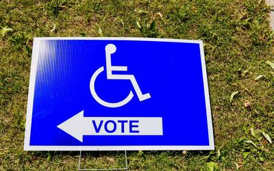A polling station sign depicts an icon of a person in a wheelchair above the word "vote."