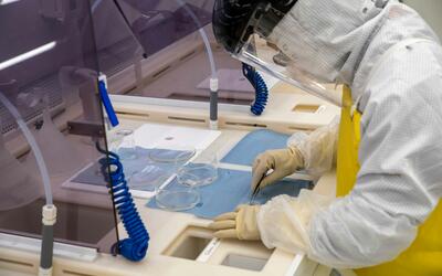 A worker in a white coverall with a yellow apron leans over a counter, using a small instrument on a flat blue material.
