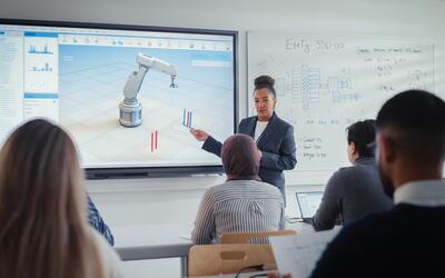 Female Professor Standing Next to Interactive Whiteboard and Teaching Diverse Students Innovations in Robotics. Computer Science and Modern Technologies in Higher Education Concept