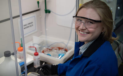 Christine McGinn wears safety glasses as she handles plastic bottles and other materials in the lab. 