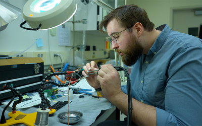 Peter Trask sits at a lab table working on wiring for a scientific device. 