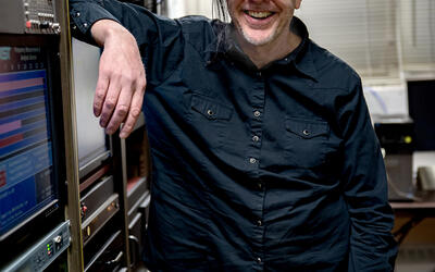 Andrew Novick poses leaning on a rack of servers and other electrical equipment.