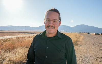 Zach Grey poses outdoors with wind turbines in the background. 