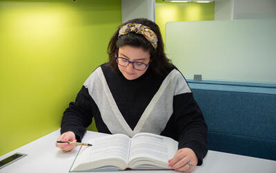 Kathryn Miller sits reading a book at a small table in the NIST library. 