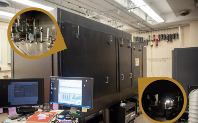 A high-tech laboratory with large black equipment featuring two circular insets showing detailed machinery setups. A computer workstation is in the foreground.