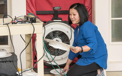 Lisa Ng kneels, holding parts of a circular fan built into a room divider. 