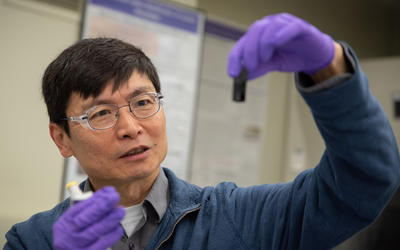 Researcher Ming Zheng looks with interest at a small vial he is holding up in front of him. 