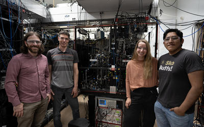 Four researchers pose standing around a large piece of scientific equipment covered with wiring and electronics. 