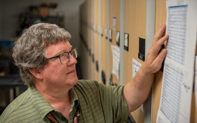 Doug White stands looking at a printed-out list taped to the end of a library shelf. 