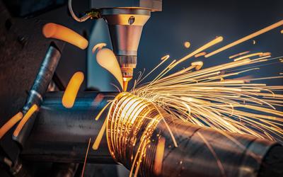 Sparks shoot off as a laser cutting head slices a metal pipe into thin circles.