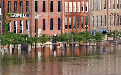 Floodwaters rise to the doorways of a row of historic brick buildings, one with a sign saying "Nashville."