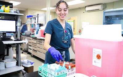 A medical worker in scrubs places a vial into a rack in a medical lab. 