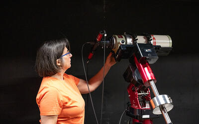 Susana Deustua looks at a large, red telescope located in a dark room. 