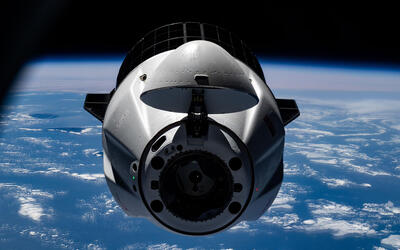 A rounded spacecraft floats in space with the blue surface of the Earth in the background.