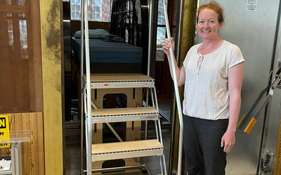 Woman poses smiling next to a set of portable stairs that lead up to a platform for an experimental MRI setup. 
