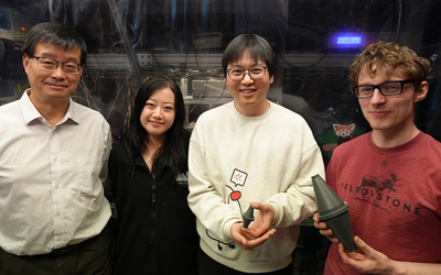 Four researchers, one older and three younger, pose in the lab holding models of a laser cavity.