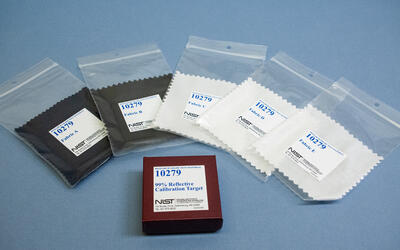 Five fabric swatches in clear plastic bags labeled 10279 are arrayed around a box labeled 99% Reflective Calibration Target. 