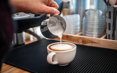 A barista pours steamed milk into a cup of espresso.