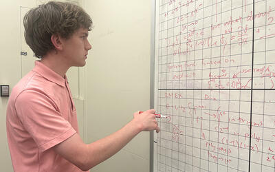 Henry Nonnemaker stands holding a marker, looking at a gridded whiteboard covered with mathematical formulas.