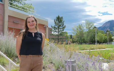 Image of a female researcher standing in front of a building with mountains in the background. 