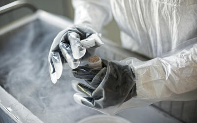 Image of a researcher wearing gloves holding a bottle of tissue material over a cart with dense fog billowing out.