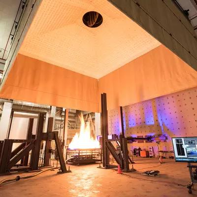 Photograph of large open room with fire engineers standing around a large fire test.