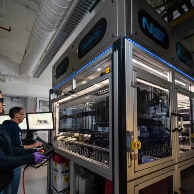 NIST researchers Elizabeth Strychalski and David Ross program the robotic arm that operates within the box-like structure of the NIST biofoundry.