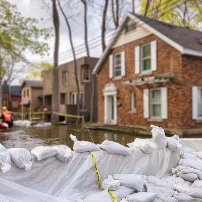 Flood protection sandbags buffer waters around flooded homes with rescue team pushing boat through flooded streets.