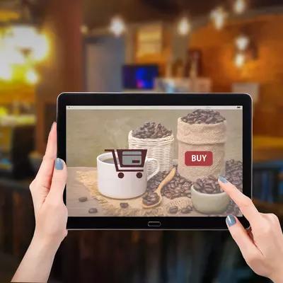 A person holds a tablet showing an online store for coffee, with coffee beans and a cup. 