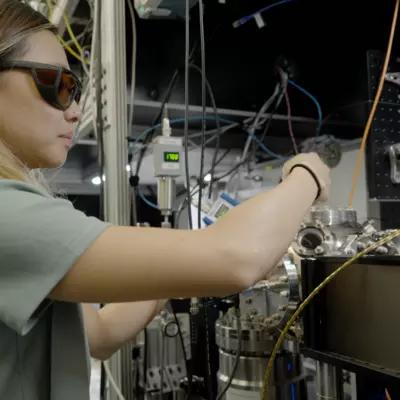 Sun Park wears safety glasses as she adjusts wiring and equipment in the lab. 