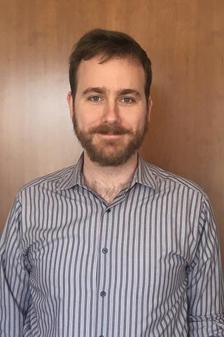 Outdated photo of John Vinson. He has brown hair and a beard, and he is wearing a vertically striped shirt.